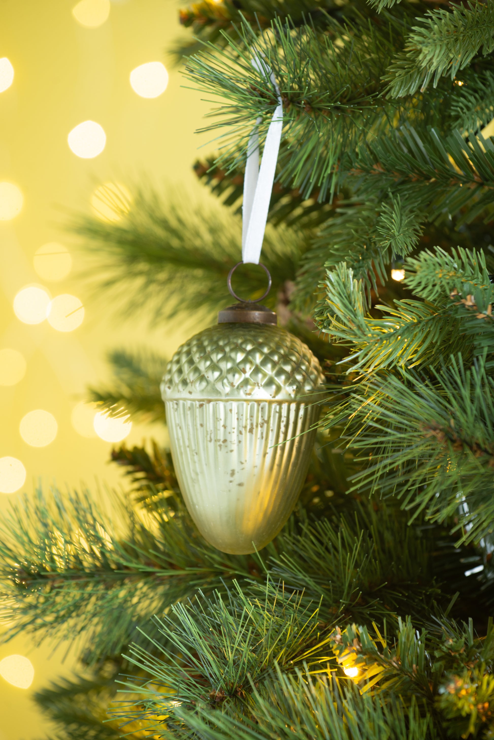 Glass acorn ornament with metallic finish hanging on a pine branch