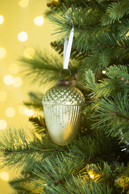 Glass acorn ornament with metallic finish hanging on a pine branch
