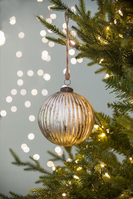 Large ribbed antique silver glass Christmas ornament hanging from pine branch