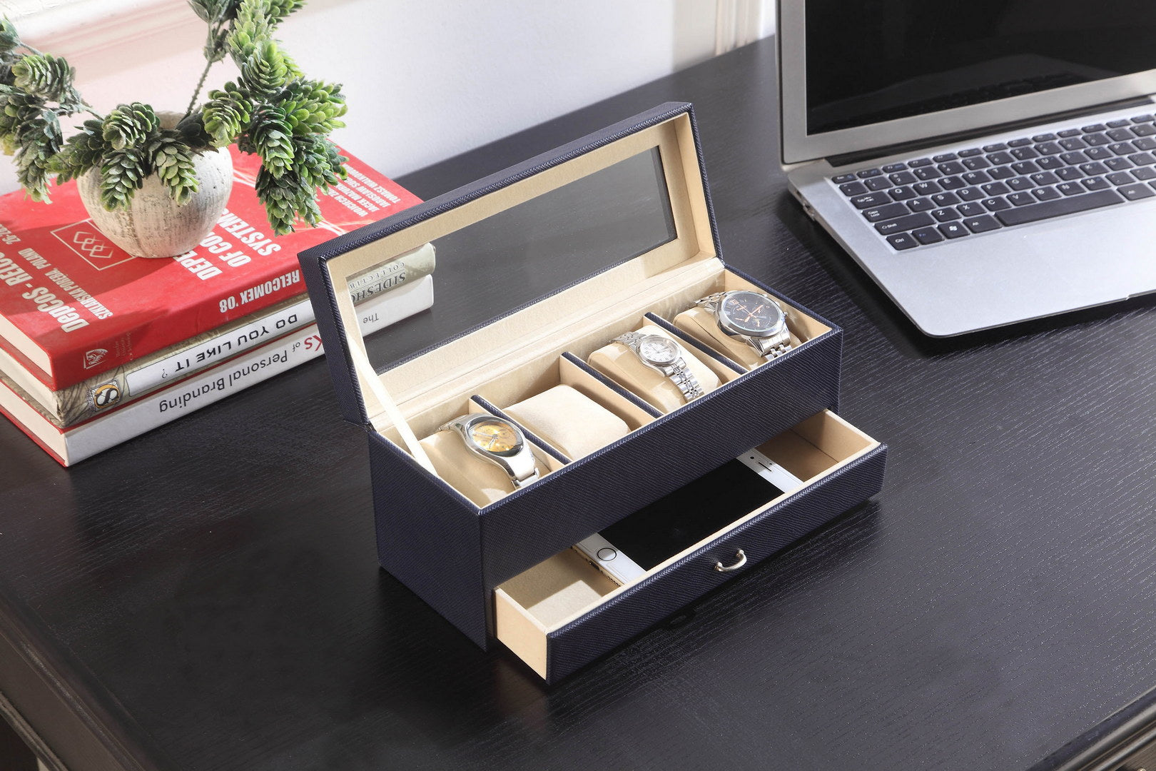 Dark blue textured watch box with four wristwatches and a smartphone