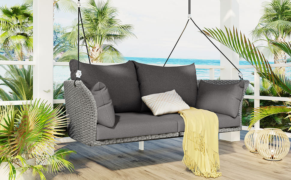 Gray wicker patio swing chair with deep cushions and yellow throw