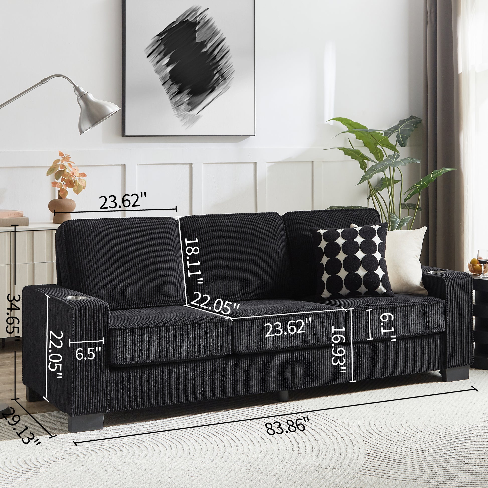 Black corduroy sofa with integrated cup holders and accent pillows on a textured rug