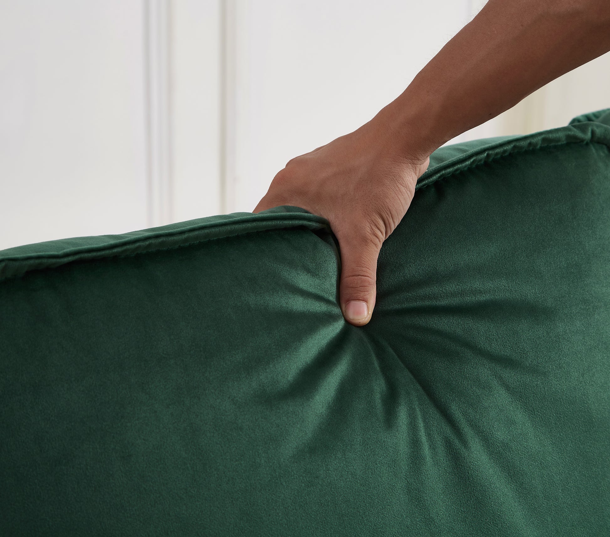 Closeup of a hand pressing into plush emerald green velvet fabric