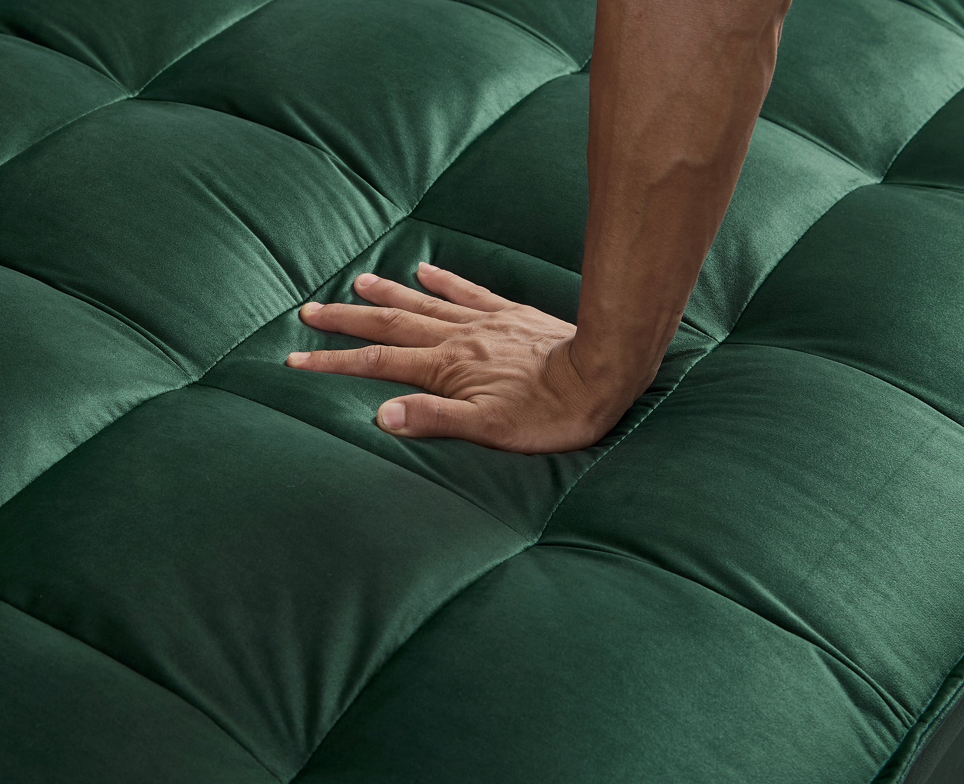 Closeup of hand pressing into tufted emerald green velvet sofa
