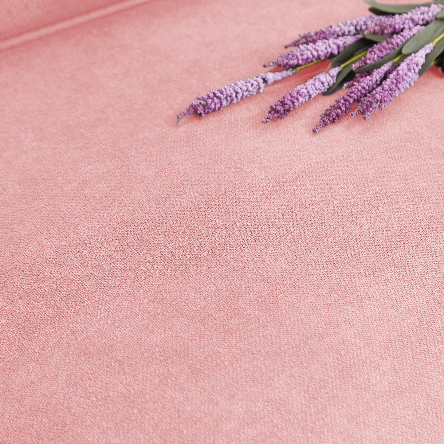 Faux lavender sprigs with purple blooms and green leaves on a textured pink fabric background