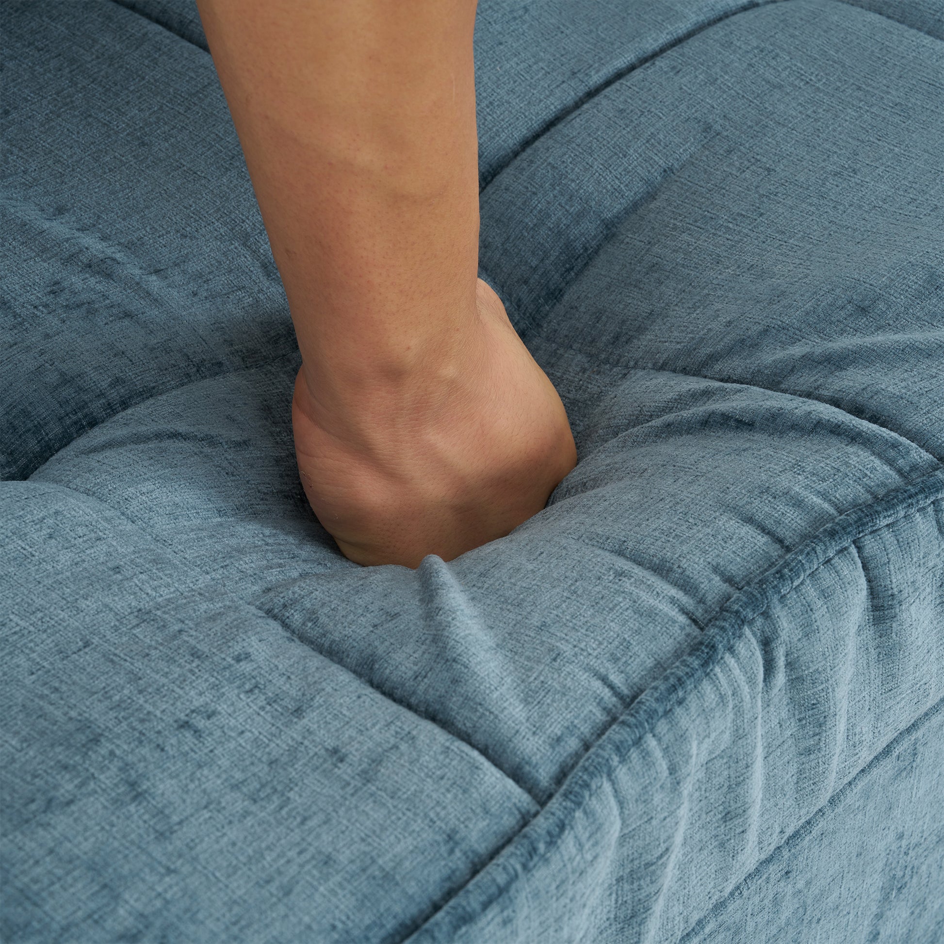 Hand pressing into plush blue linen tufted sofa cushion