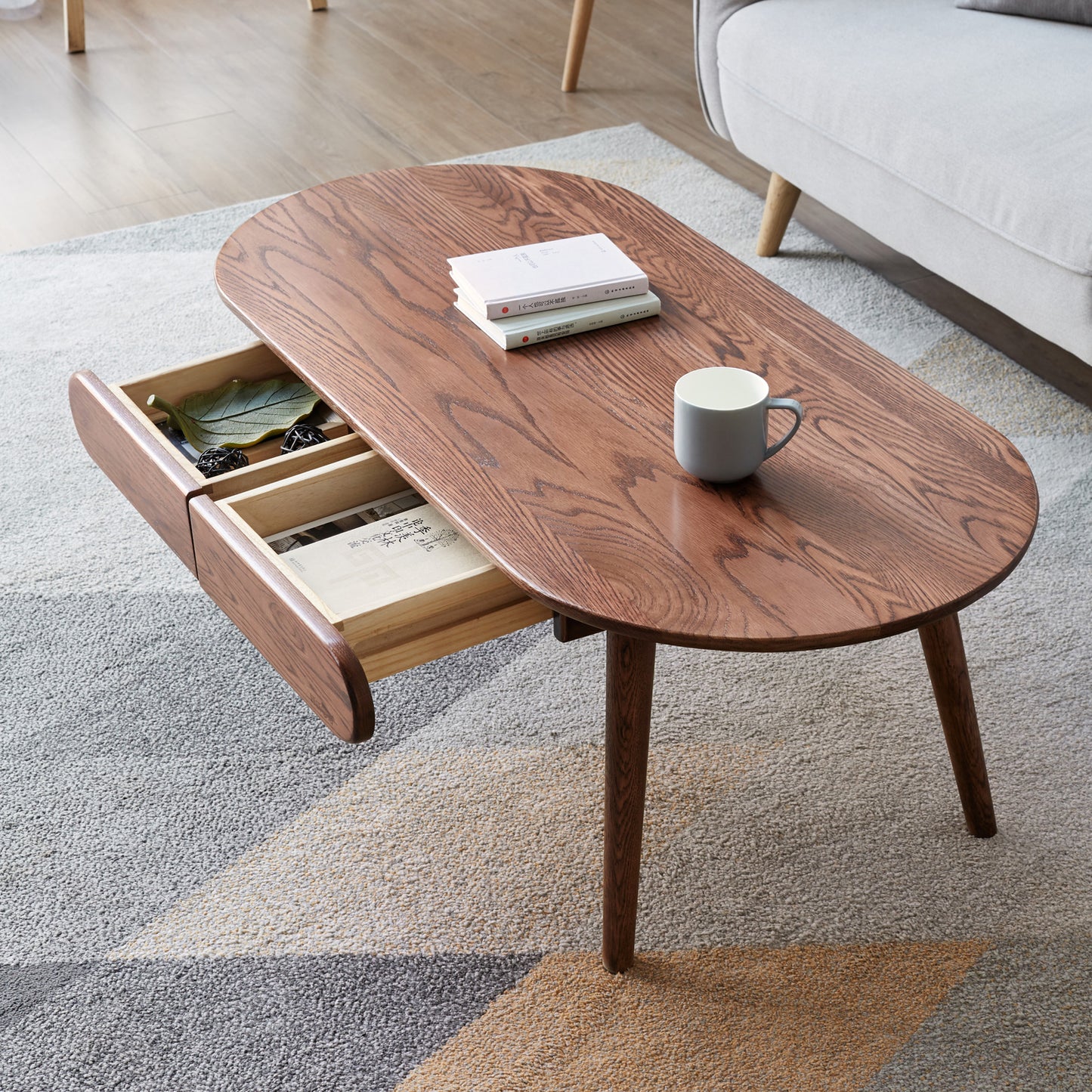 Oval oak coffee table with two pullout drawers and a grey mug