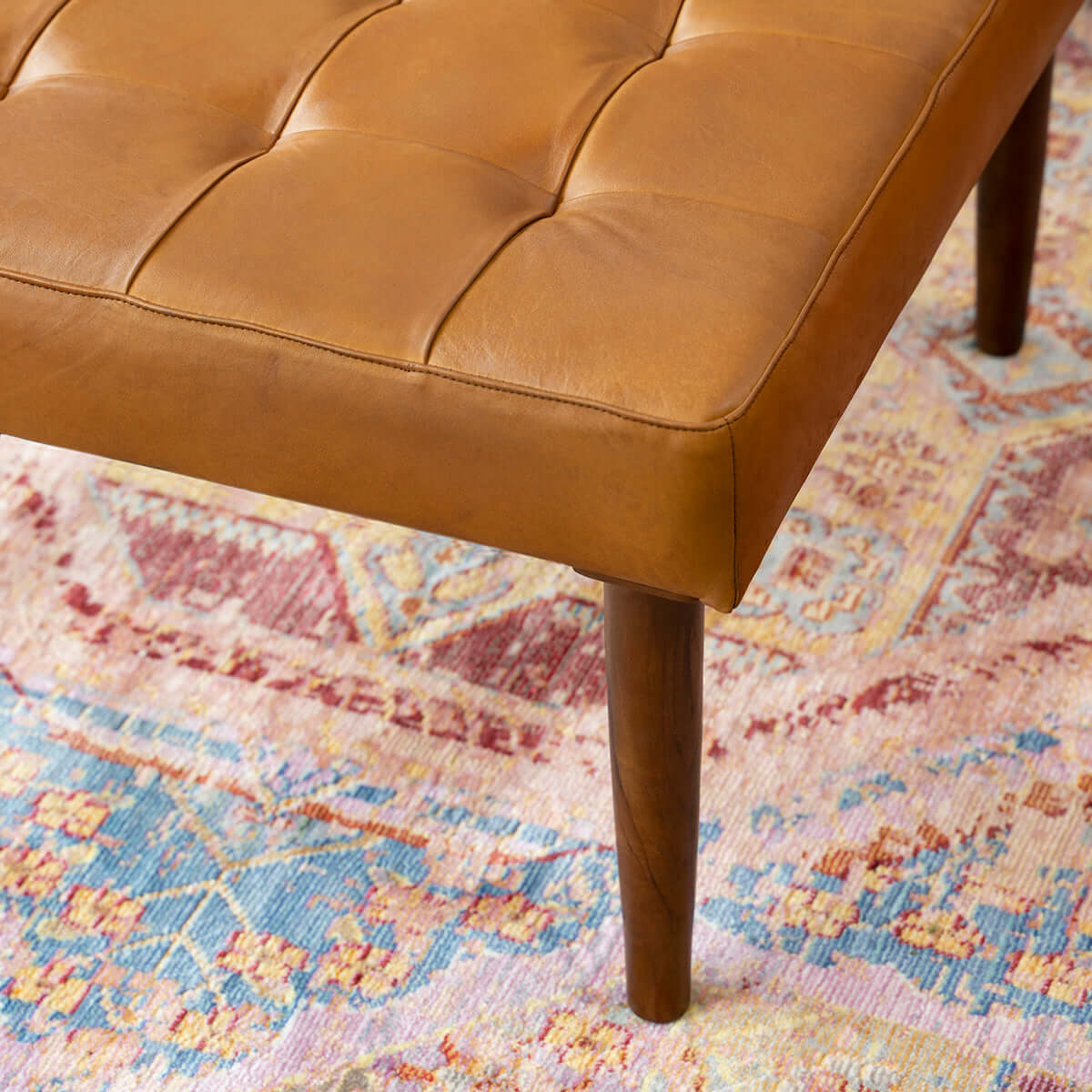 Tufted tan leather ottoman with tapered wooden legs on a vintage rug