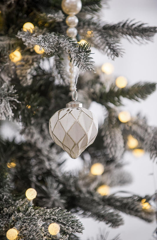 White diamondpatterned glass Christmas ornament hanging on a flocked tree branch