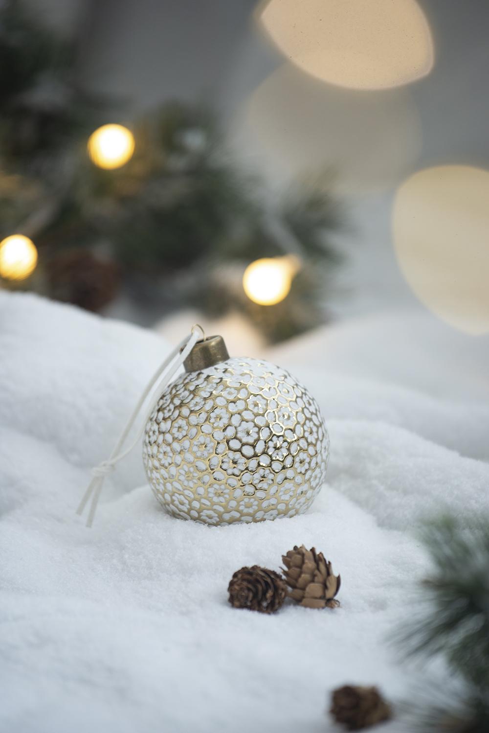 White and gold ornate Christmas bauble with embossed floral pattern on snowy background