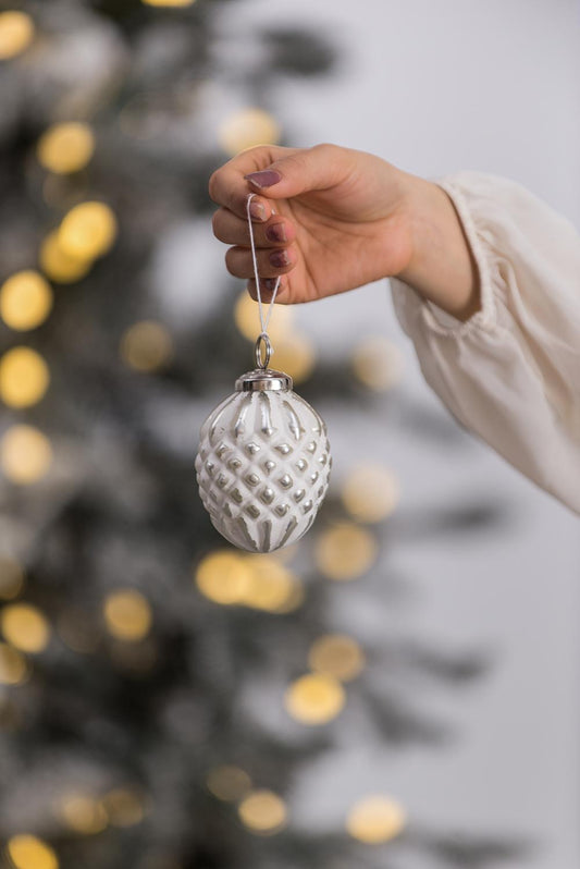 White textured pinecone Christmas ornament held by a hand