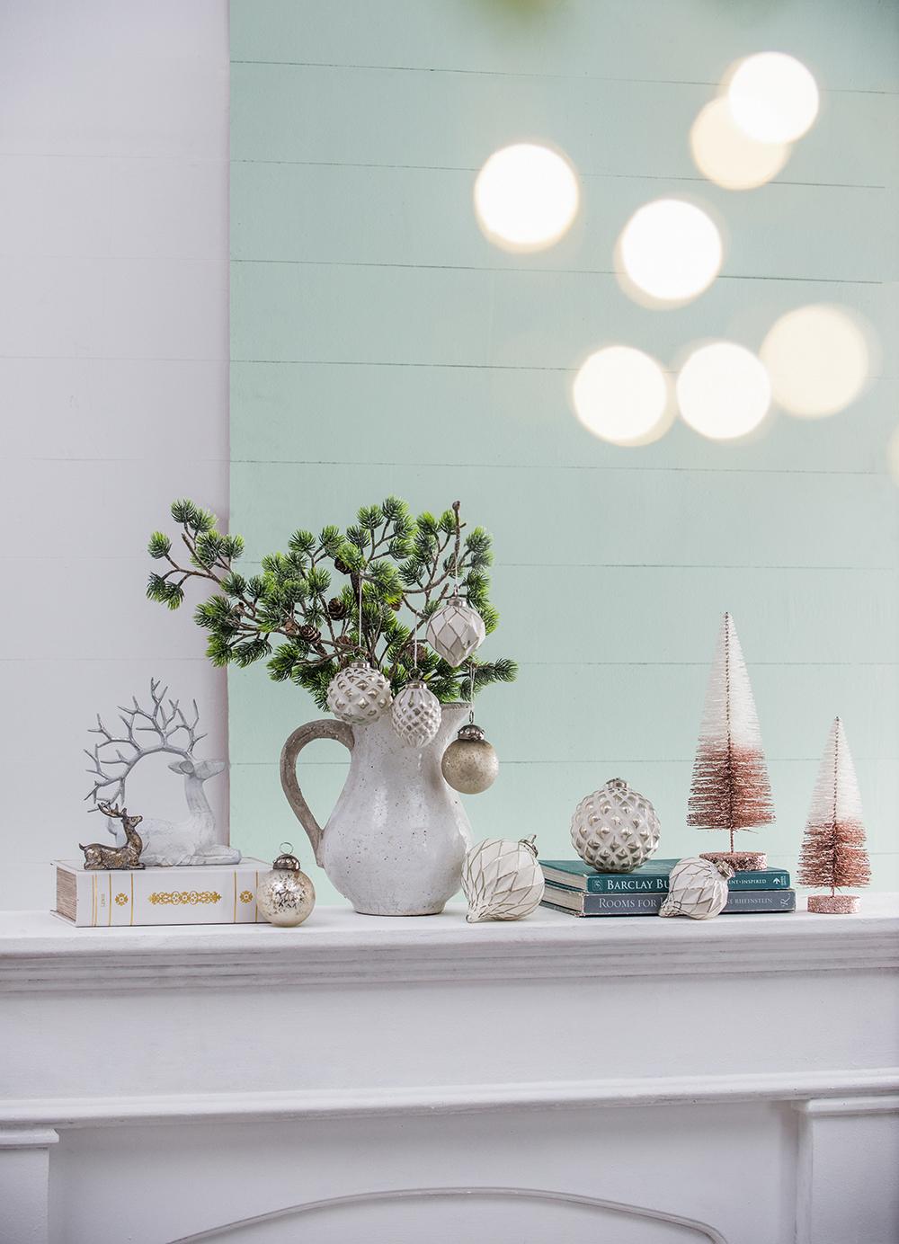 White ceramic pitcher filled with pine branches and white Christmas ornaments