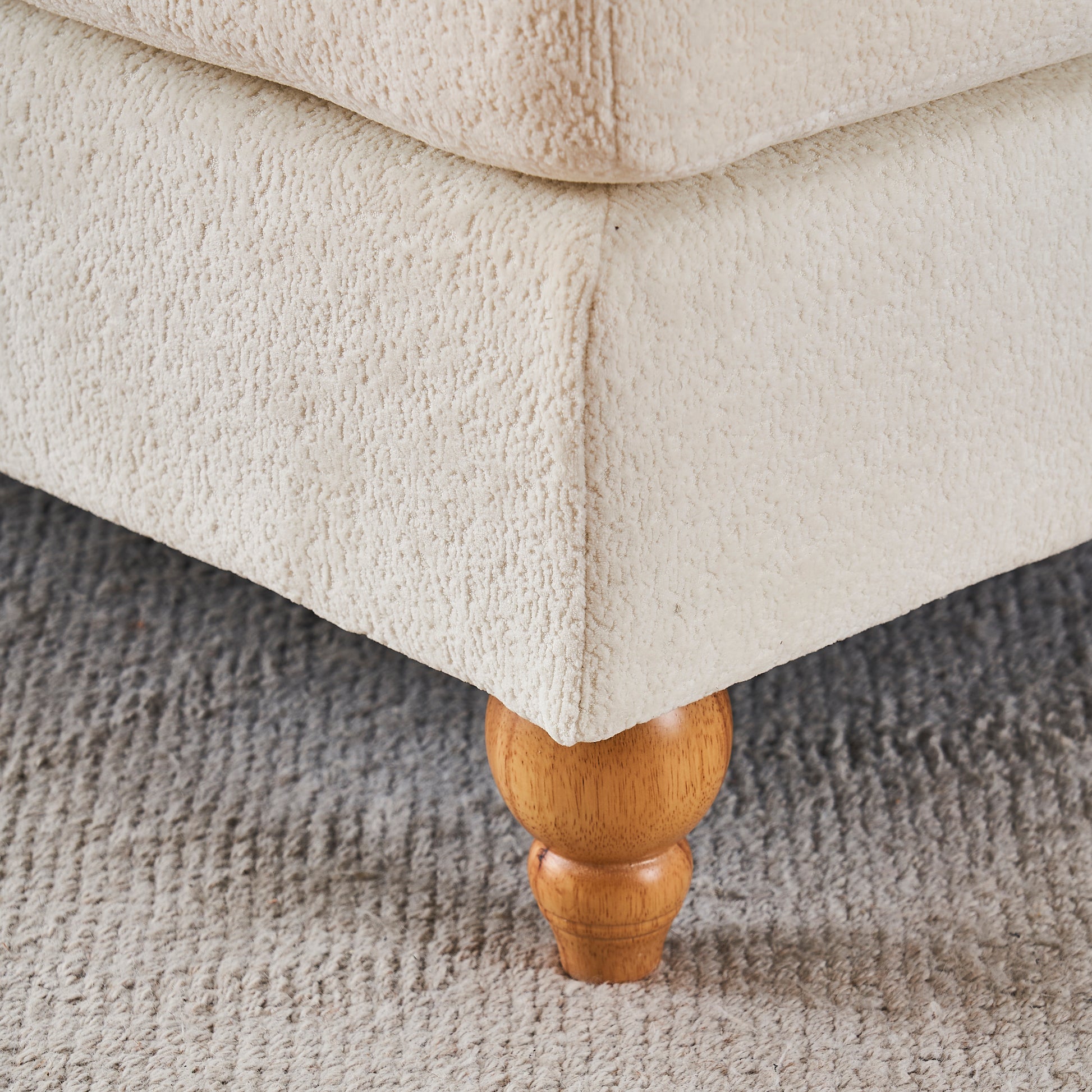 Cream boucle fabric sofa corner with turned wooden leg on grey rug