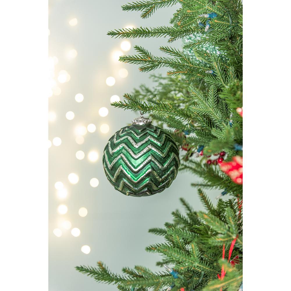 Shiny green glass Christmas ornament with silver chevron pattern hanging on a tree