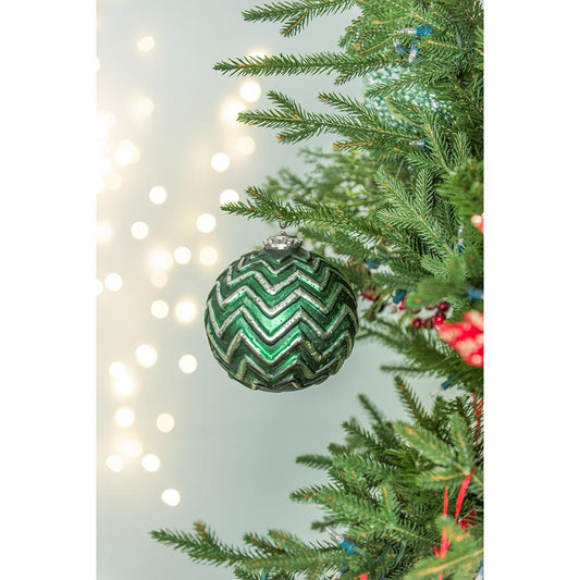 Shiny green glass Christmas ornament with silver chevron pattern hanging on a tree
