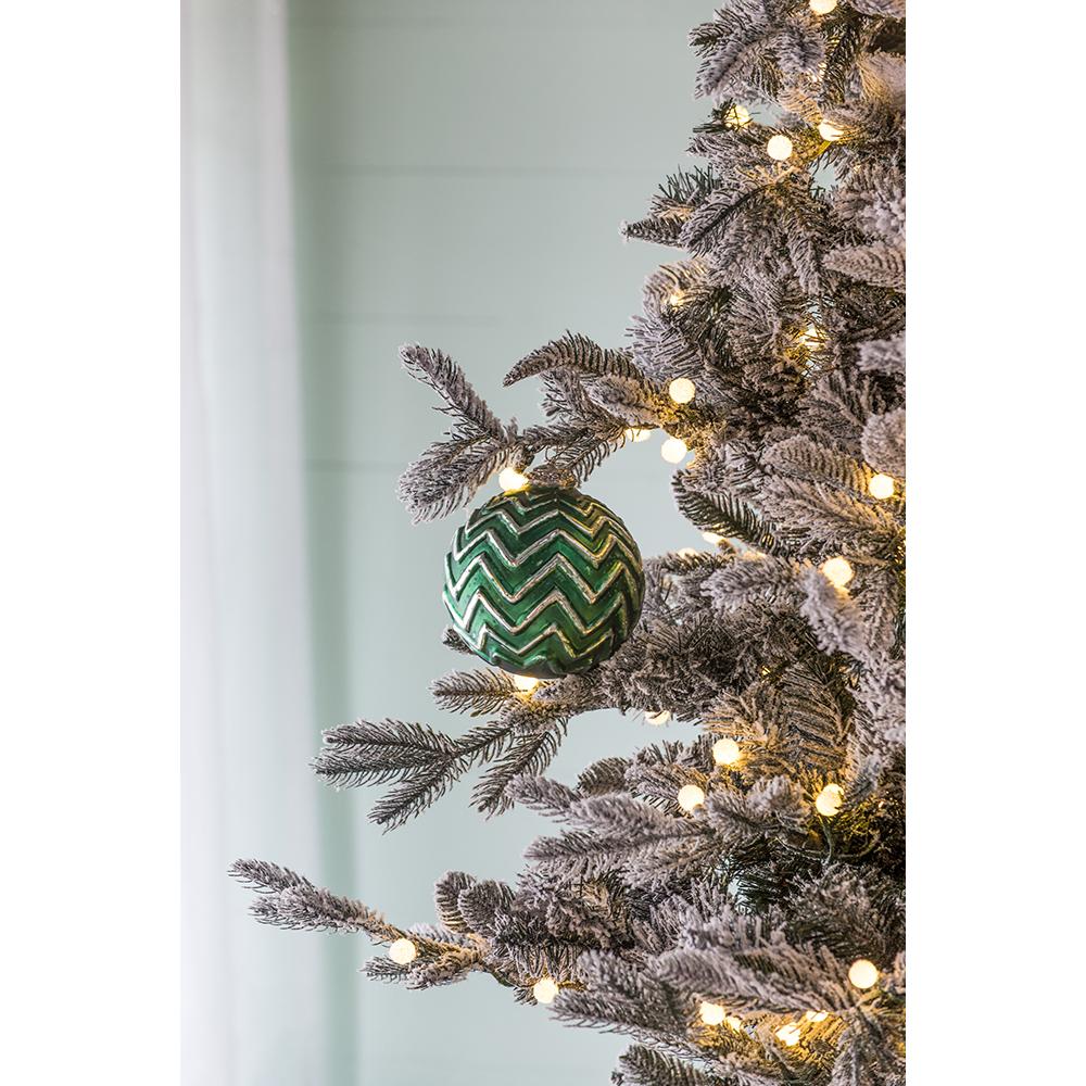 Green patterned Christmas ornament hanging on a flocked tree branch