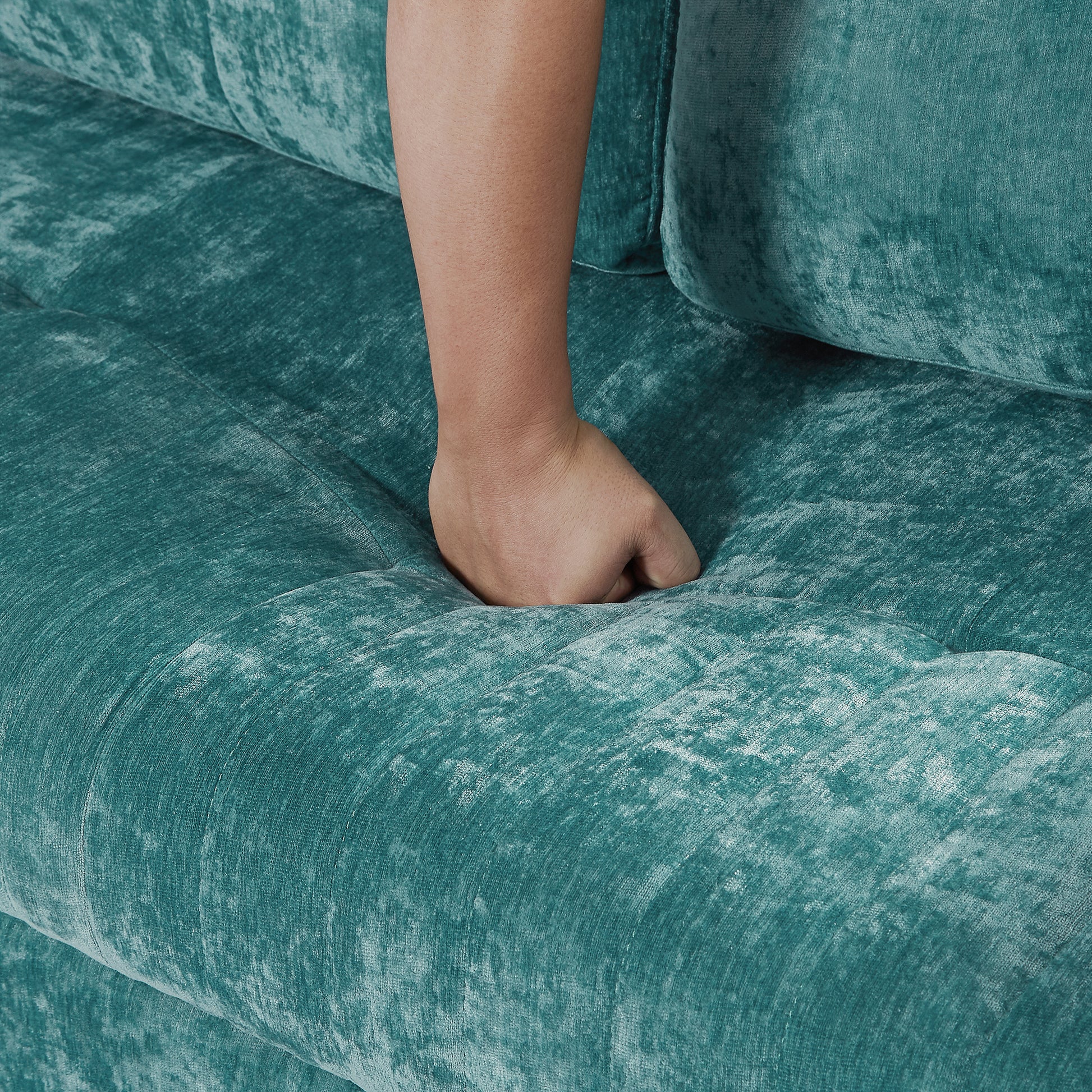 Closeup of plush teal velvet sofa cushion with hand sinking in showing soft texture
