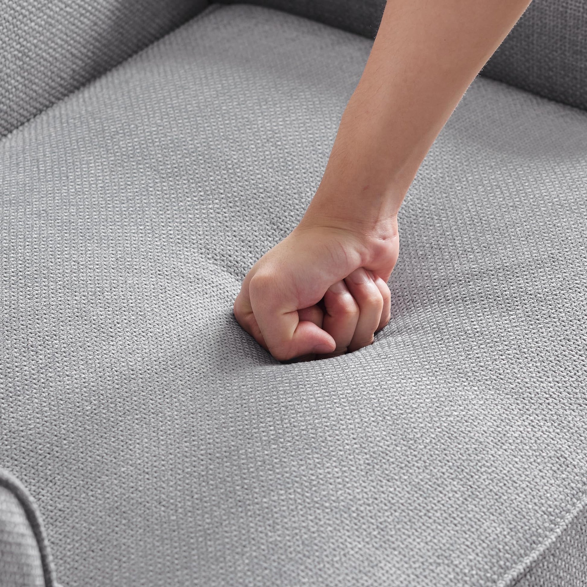 Closeup of a hand pressing into plush grey fabric upholstery showcasing sofa comfort