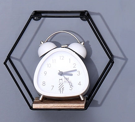 White analog alarm clock with dual bells on a wooden shelf within a black hexagonal wall mount