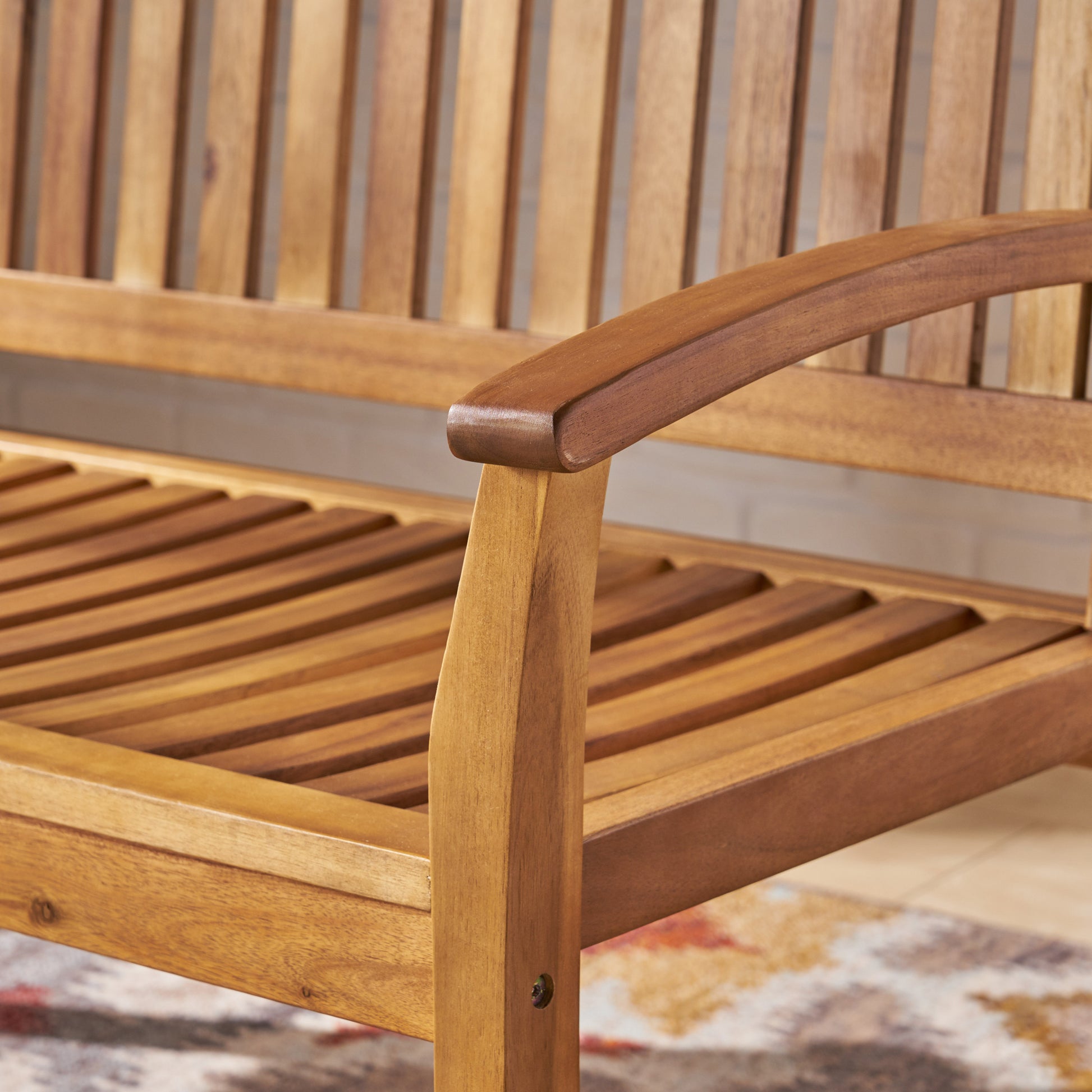 Closeup of a warmtoned wooden garden bench with slatted seat and curved armrests