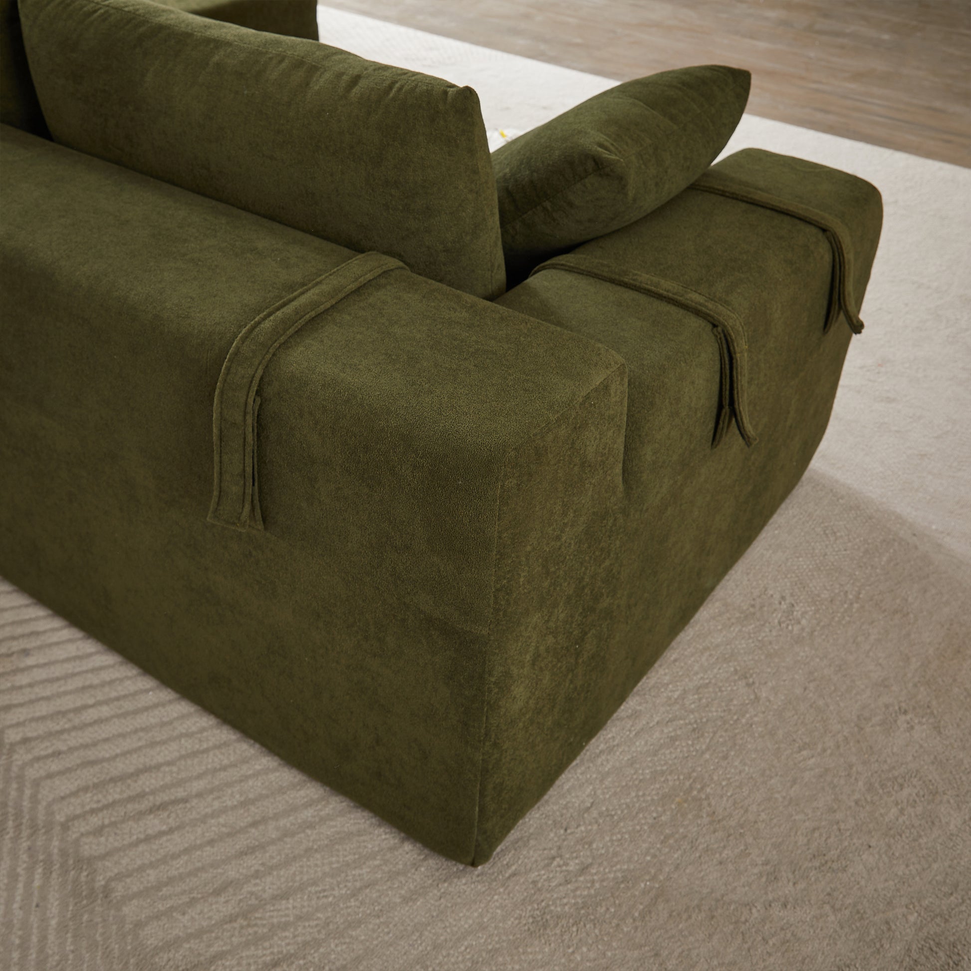 Dark green fabric sectional sofa corner with plush cushions and decorative strap details