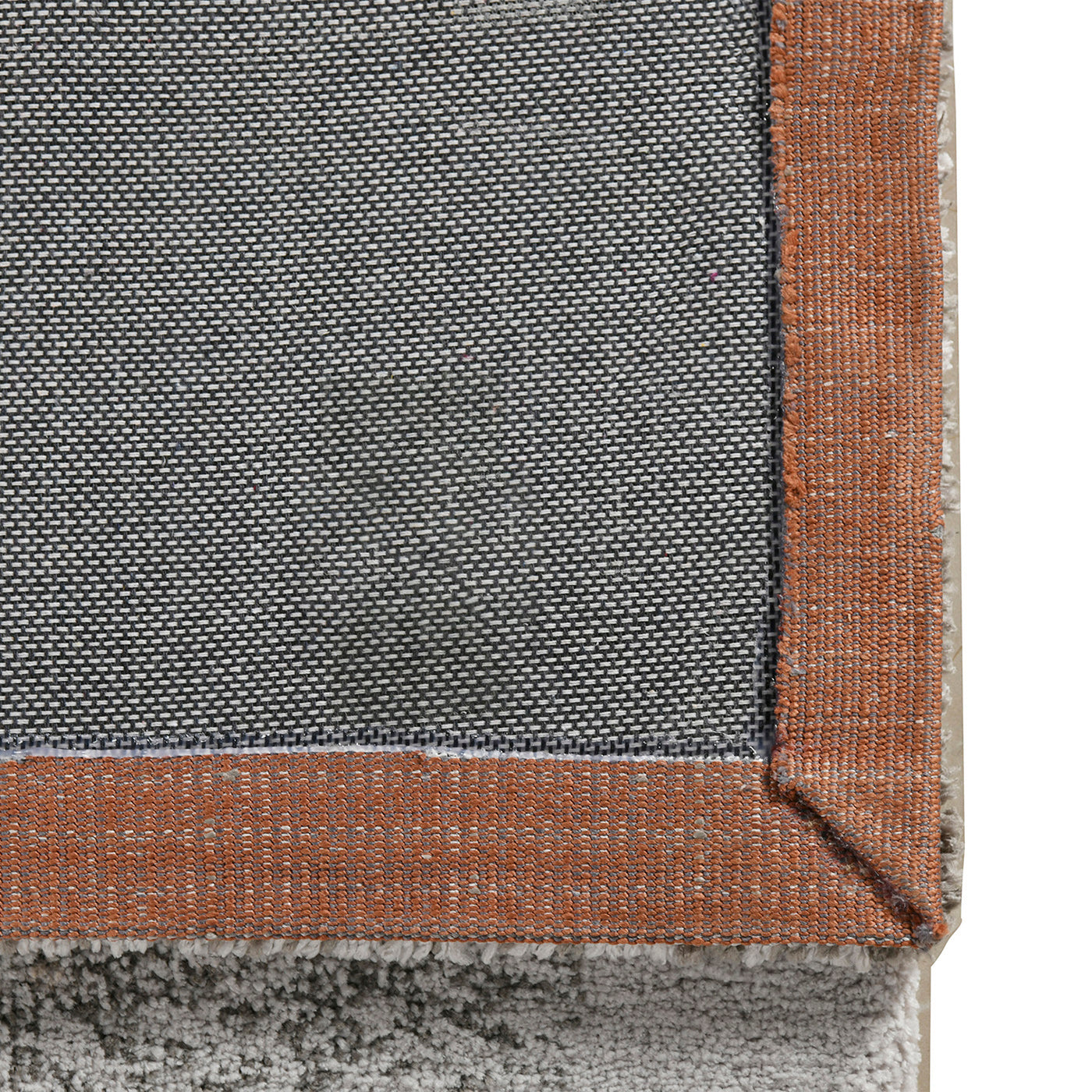 Closeup of textured grey rug backing with orange binding