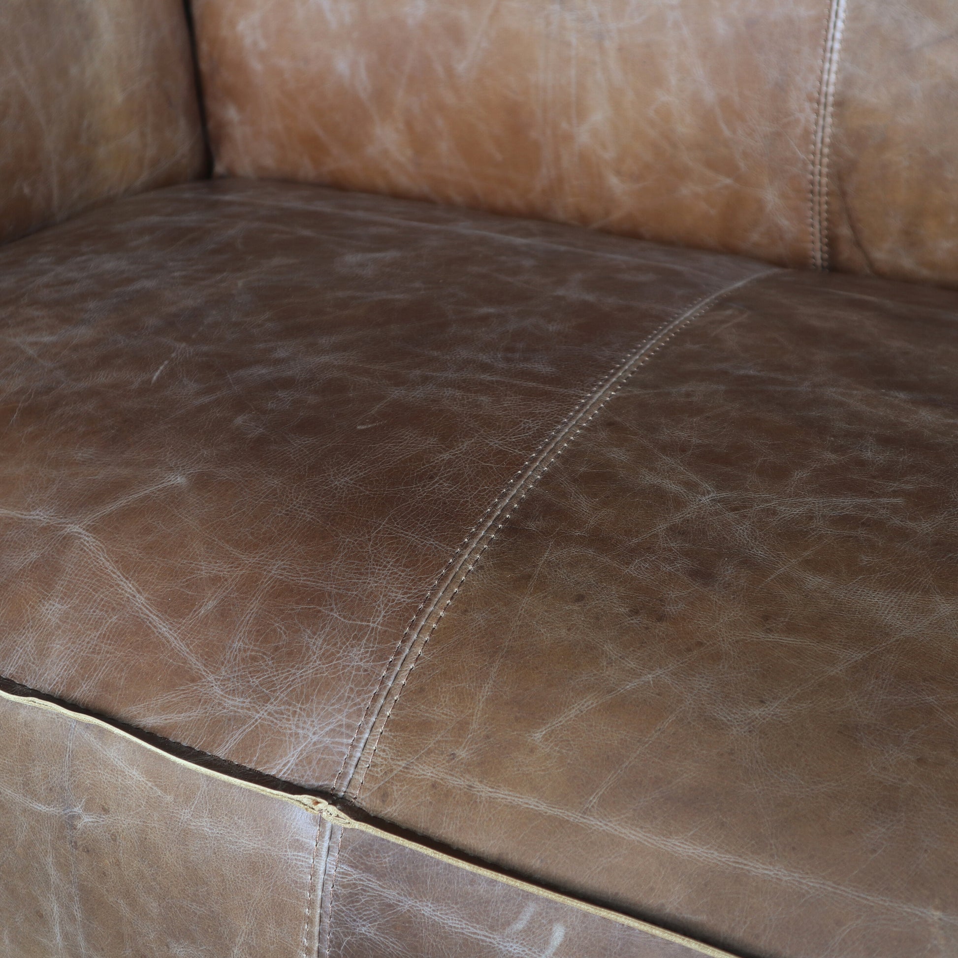 Closeup of distressed brown leather sofa cushions with detailed stitching and natural texture ideal for rustic home decor