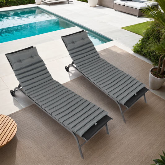 Two grey padded chaise lounges with adjustable frames on a patio by a pool