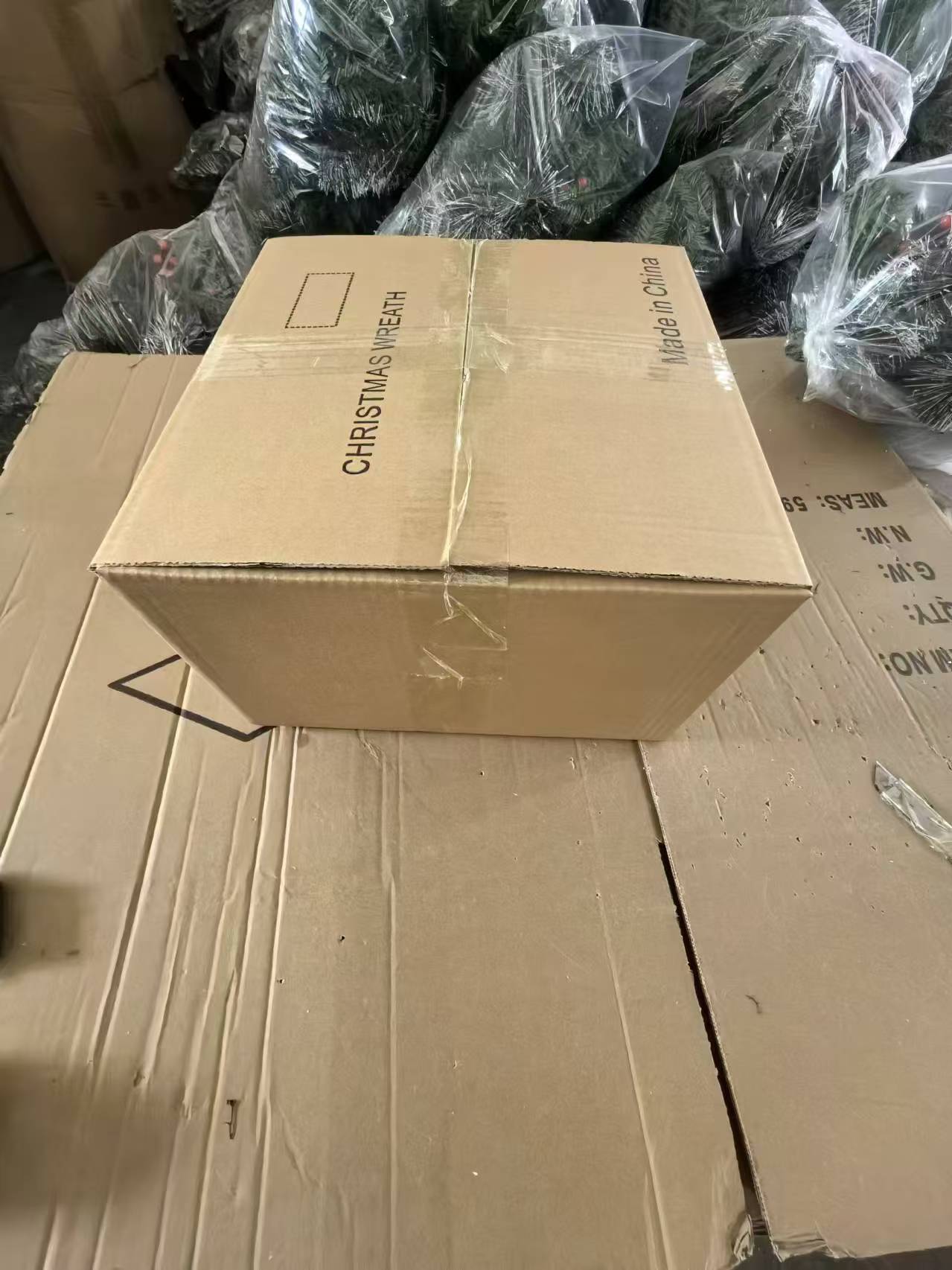 Cardboard box labeled Christmas Wreath with multiple plasticwrapped artificial wreaths stacked around it