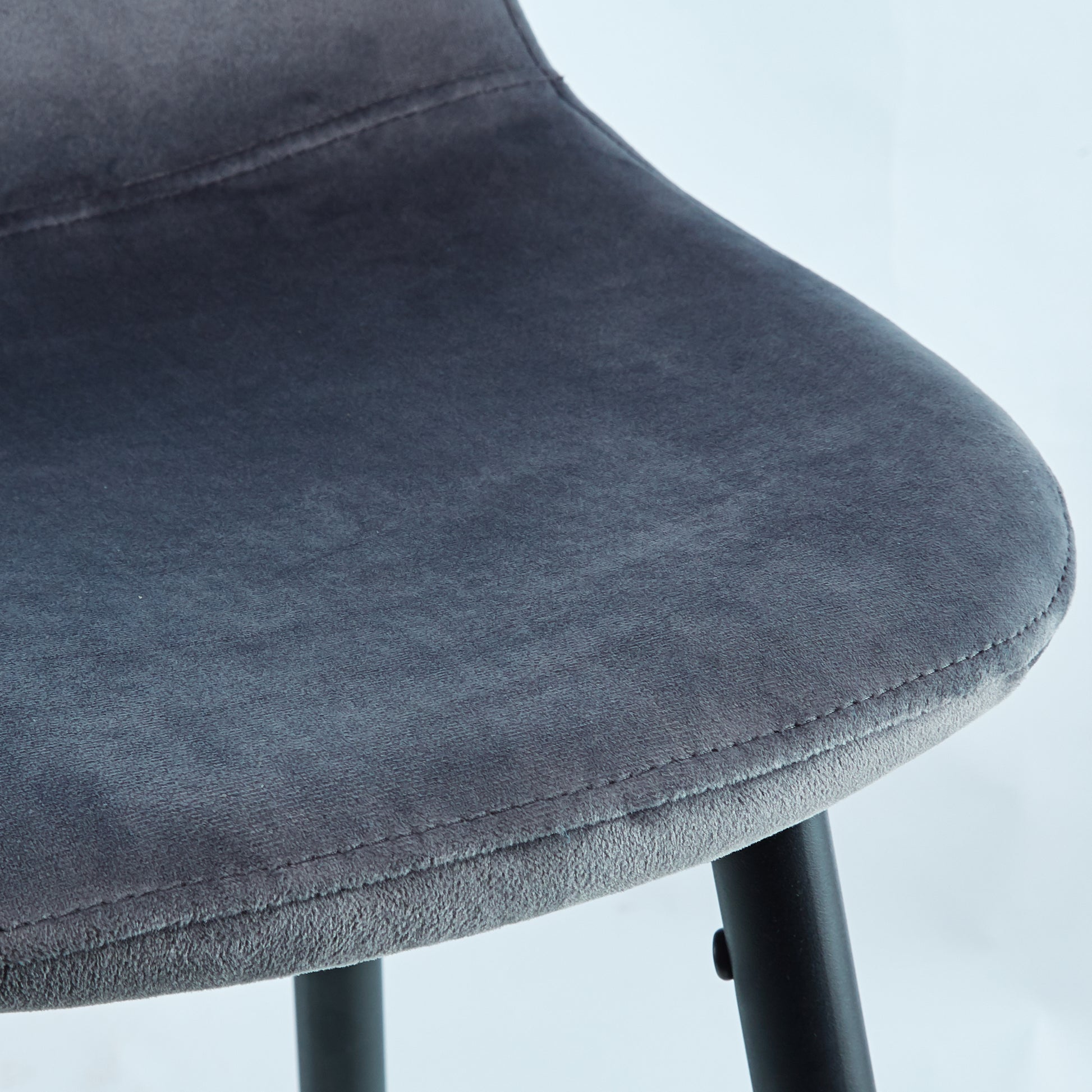 Closeup of a dark gray velvet bar stool seat with detailed stitching and black metal legs