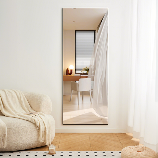 Tall black framed floor mirror reflecting a modern interior with desk and chair