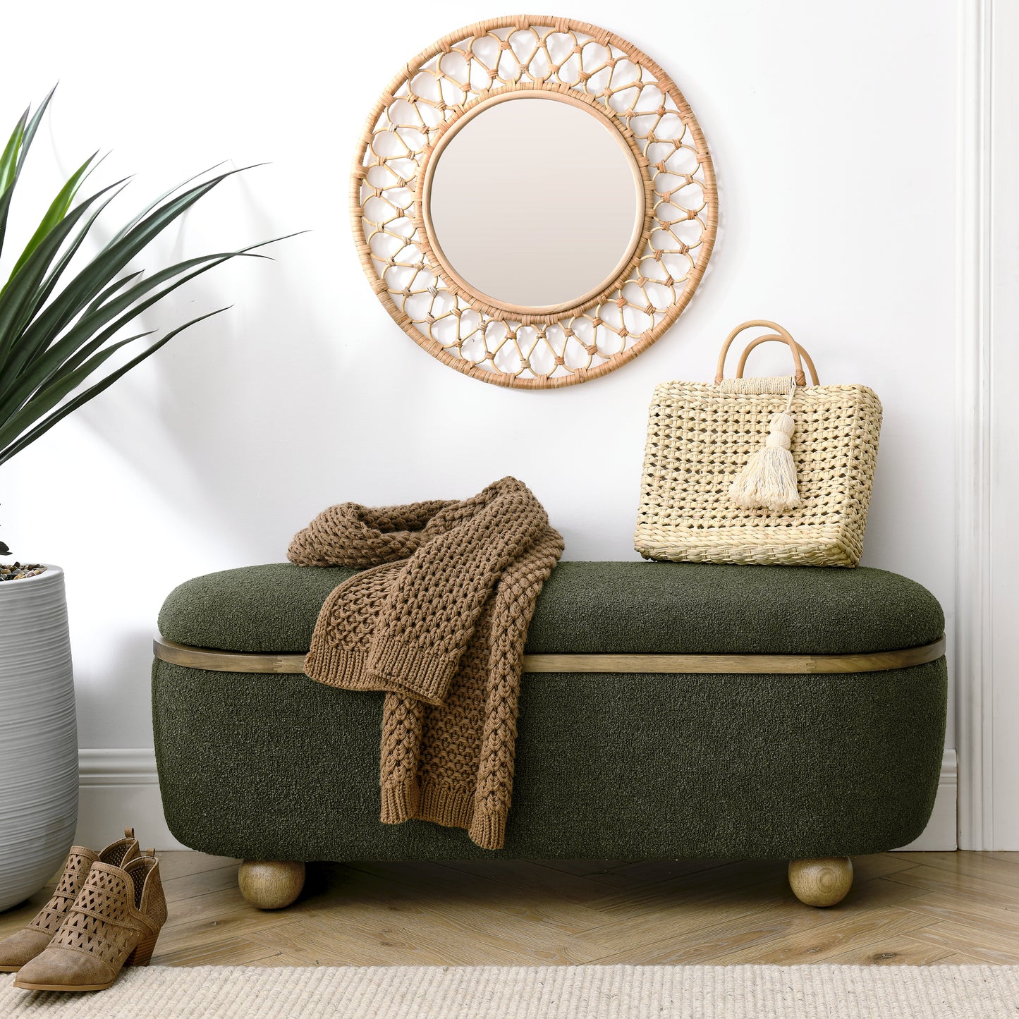 Green upholstered storage ottoman with wooden legs and a knit blanket draped over it
