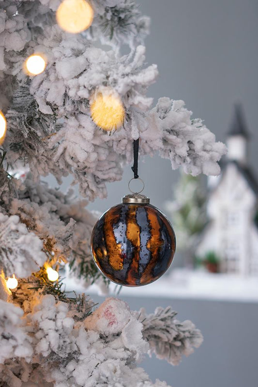Amber and charcoal striped glass Christmas bauble hanging on a flocked tree