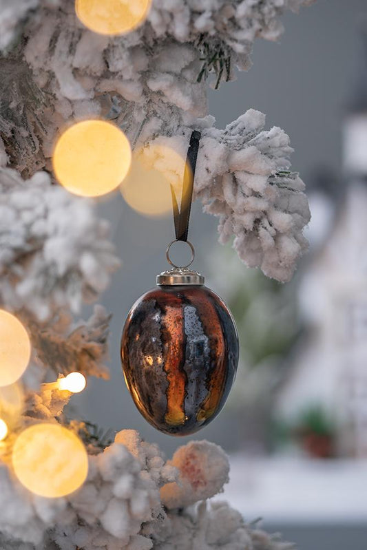 Shimmering striped antique glass Christmas ornament in bronze and black hanging on a frosted tree branch