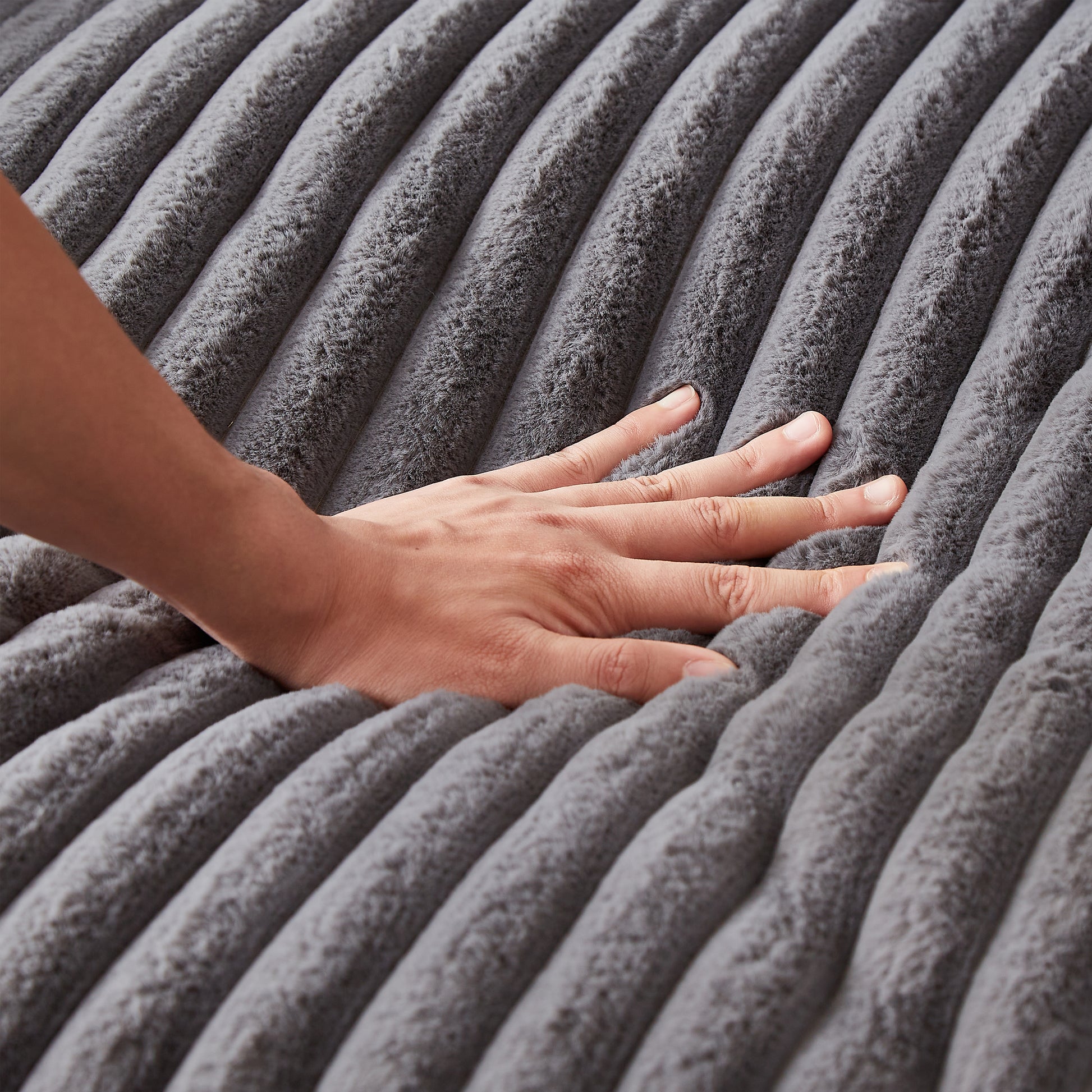Closeup of a hand pressing into a plush gray ribbed blanket for comfort