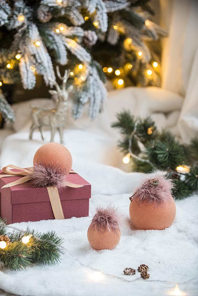 Fluffy pink baubles sit on snowcovered ground next to a rose gift box with ribbon