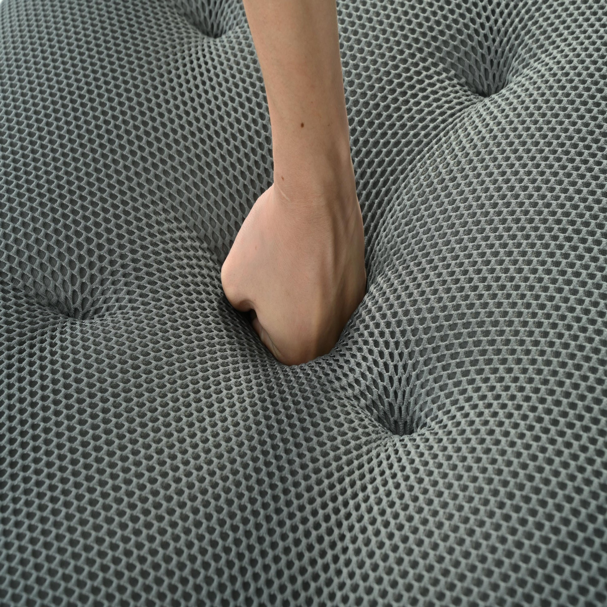 Closeup of hand pressing into grey breathable mattress fabric showing plush comfort