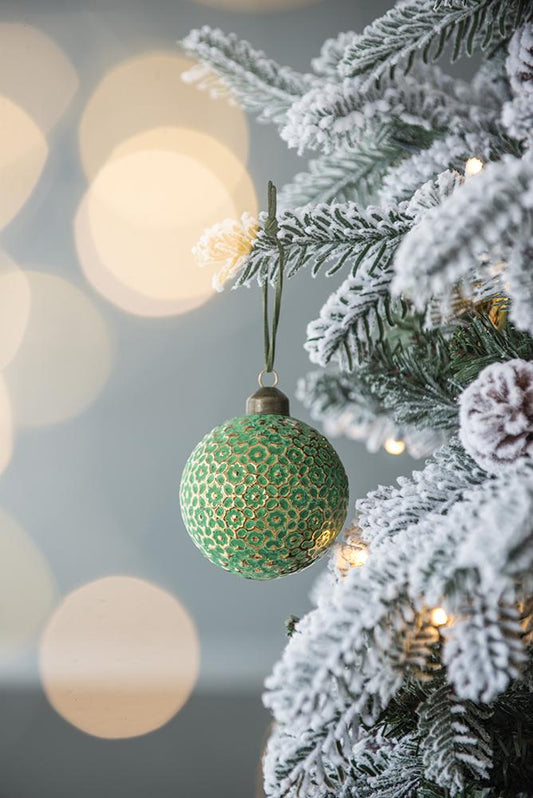 Green ornate Christmas bauble hanging on a flocked tree branch