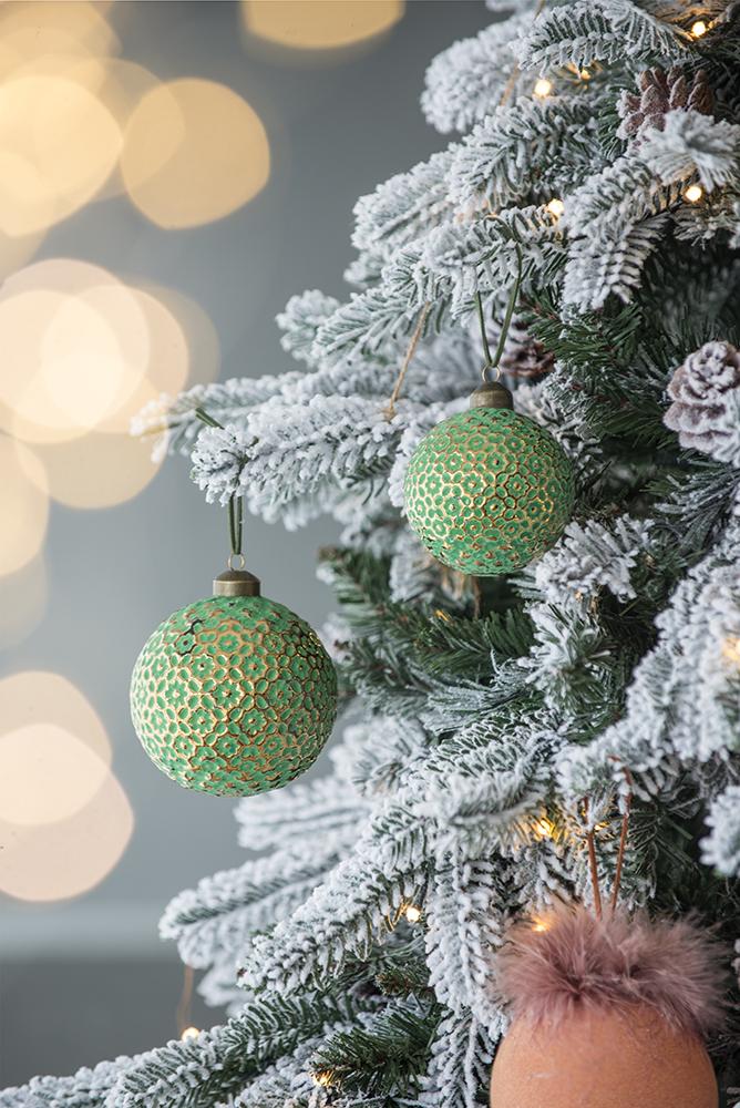 Textured green Christmas ornament with gold floral pattern detail hanging on flocked tree branch