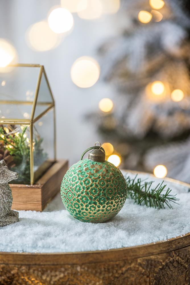 Textured green glass Christmas ornament with gold accents on faux snow