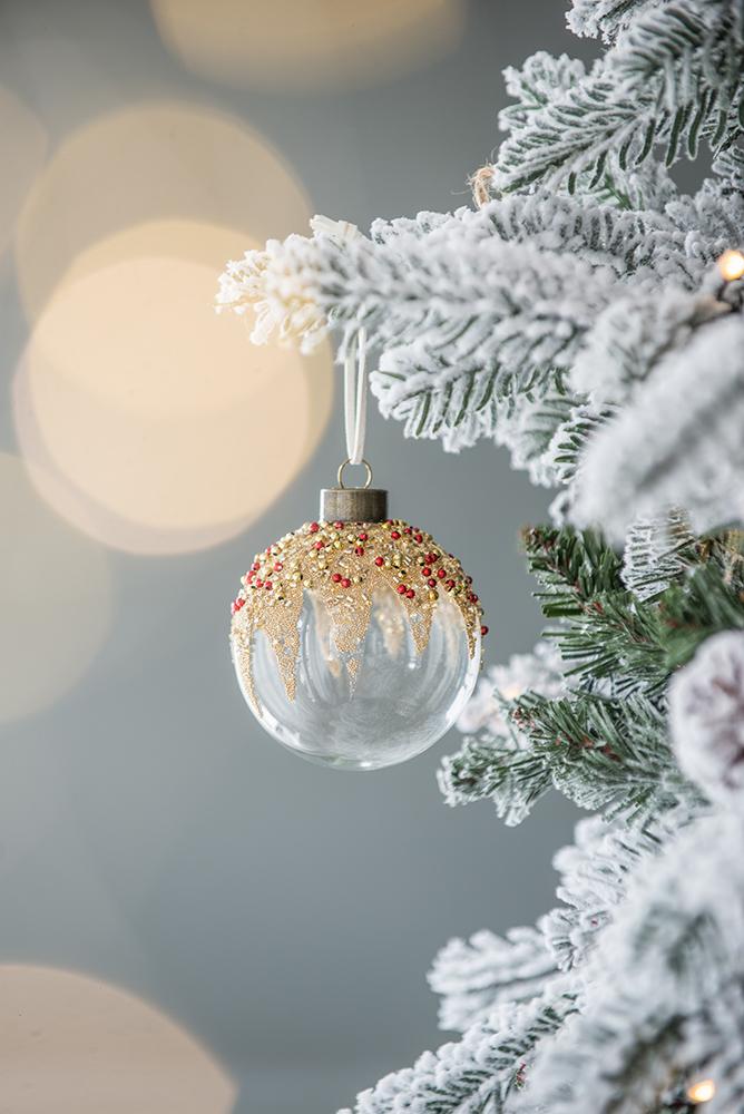 Clear glass Christmas ornament with red and gold beaded detail hanging on flocked branch