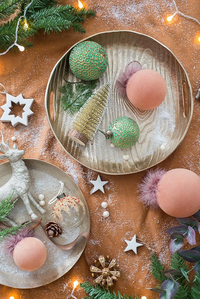 Green textured Christmas baubles with gold accents on a rustic tray part of festive decor