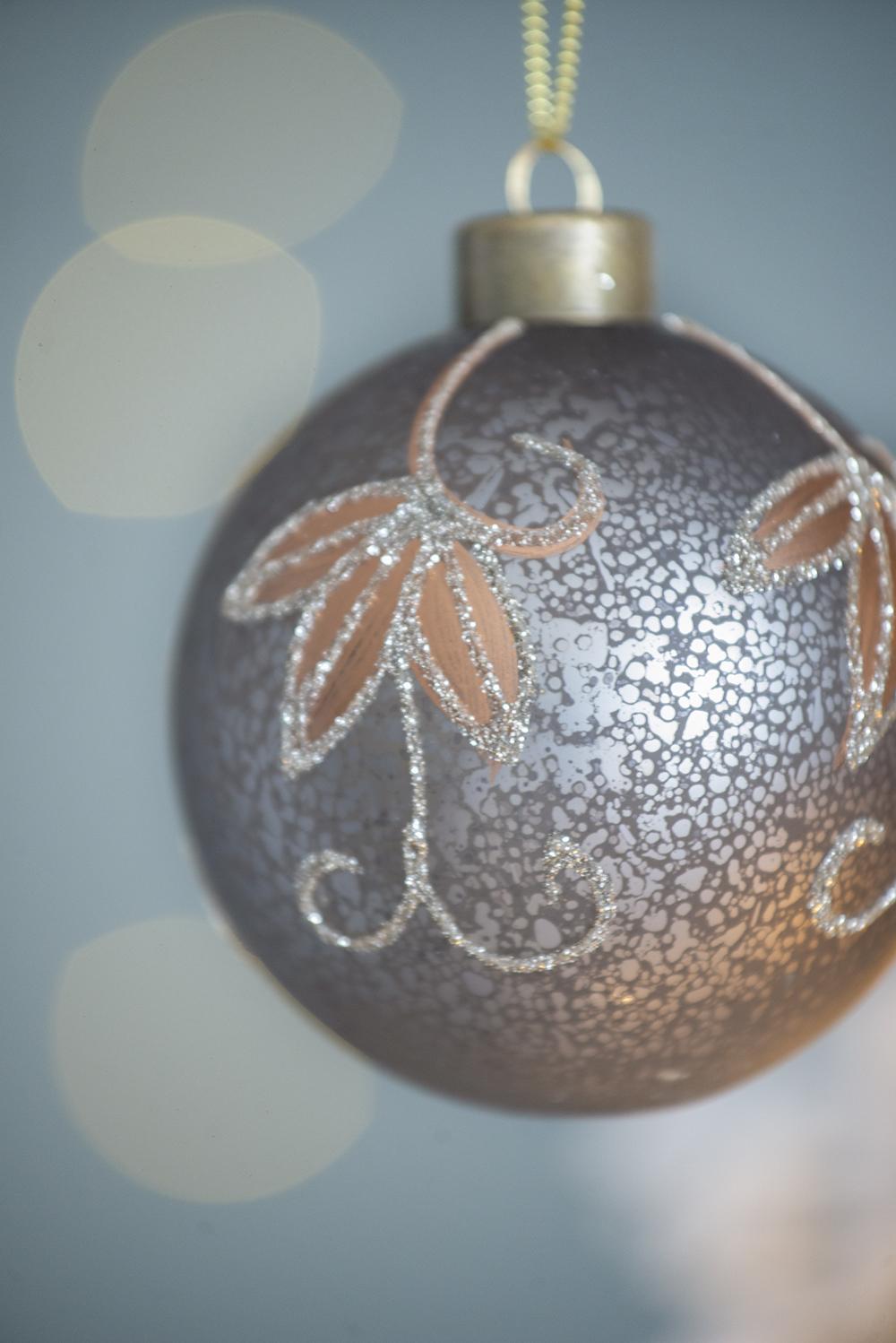 Frosted gray Christmas ornament with ornate copper leaf and glitter scroll design
