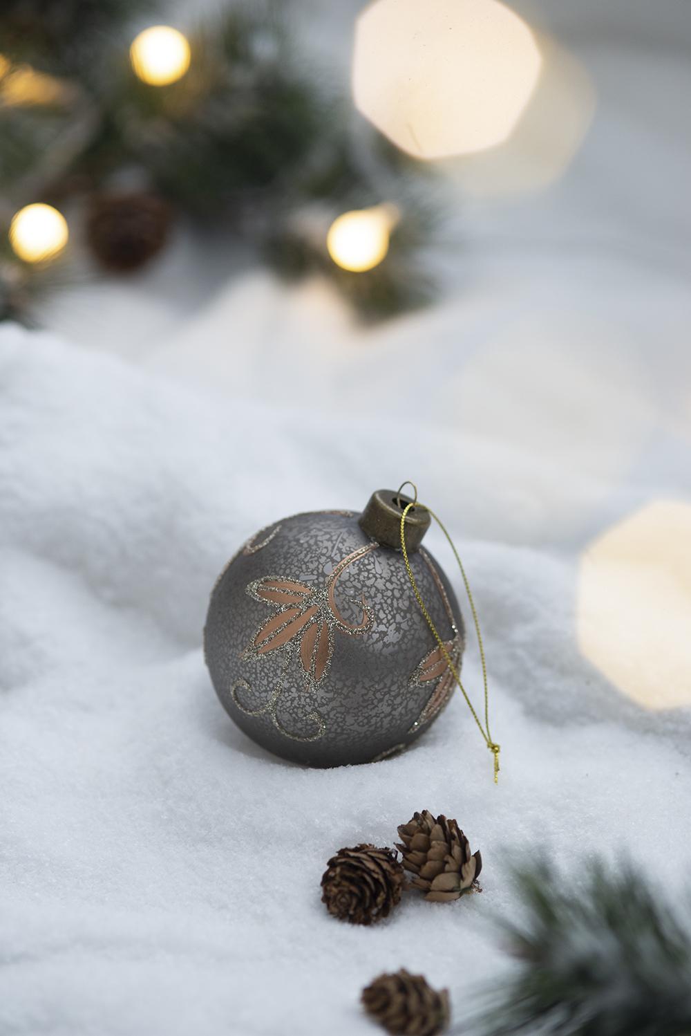 Grey glass Christmas ornament with gold leaf pattern on snowy background