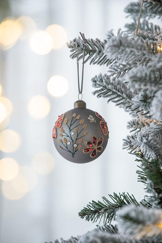 Gray glass Christmas ornament with red floral sequins and gold glitter accents hanging on a frosted tree branch