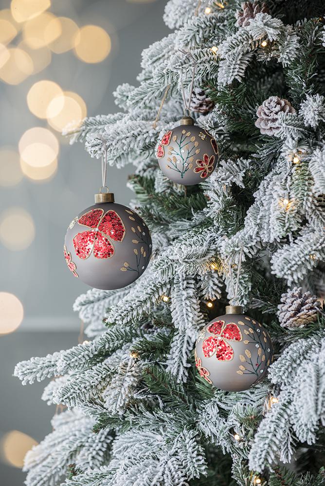 Grey Christmas ornament with red glitter floral design hanging on frosted tree branch