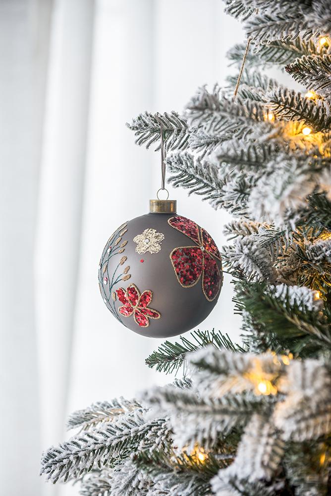 Gray Christmas ornament with red floral glitter detail hanging on a flocked tree branch