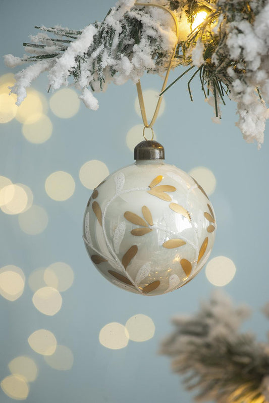 Frosted glass Christmas ornament with gold leaf pattern hanging on a snowy tree branch