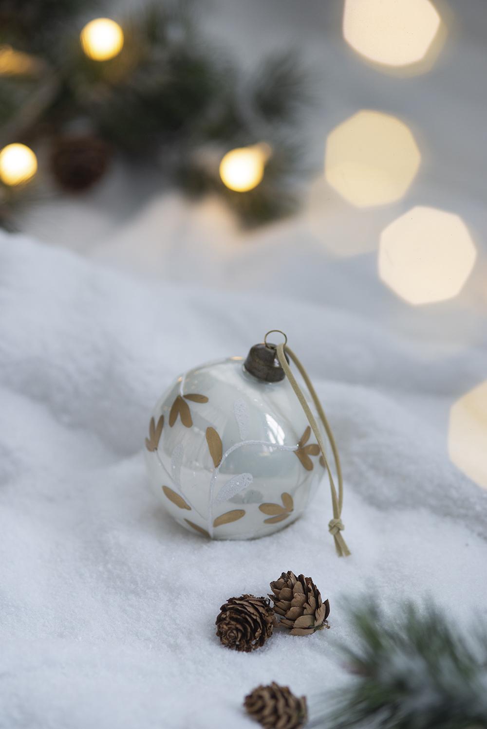 White glass Christmas ornament with gold leaf design nestled in snow