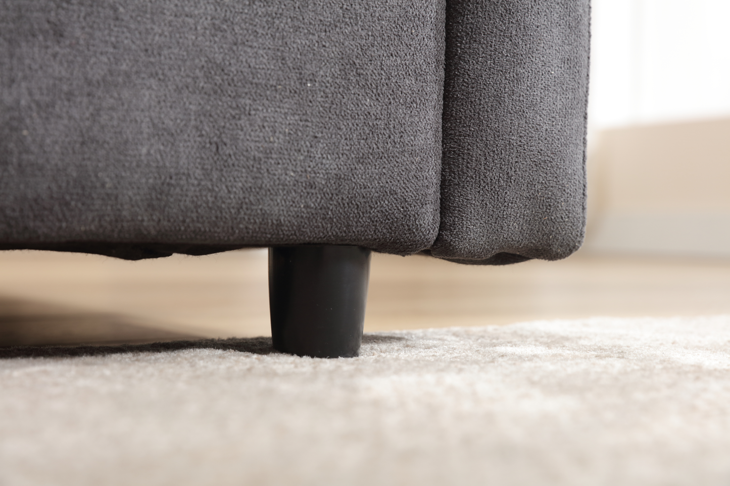 Closeup of a dark gray textured fabric sofa leg on a light beige rug